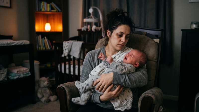 Exhausted mother holding an unsettled crying baby in a dim nursery at 2am — 4-month sleep regression